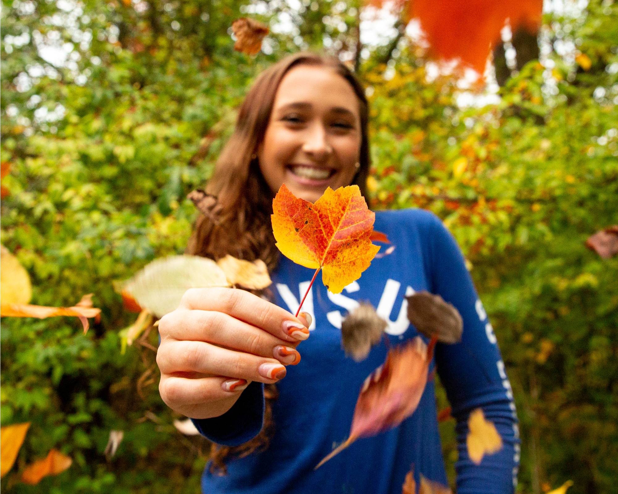 Person holding a fall leaf while on a hike
